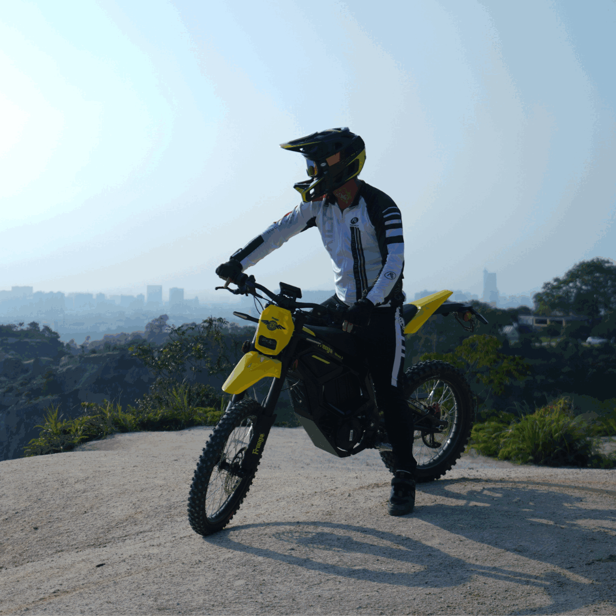 Rider on Freego Nova 5 electric dirt bike overlooking city from a cliff edge